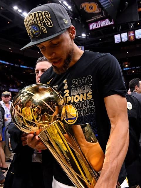 Curry in a 2018 back-to-back champions shirt holding the trophy